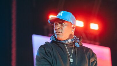 Rapero con gorra azul y micrófono en la mano sobre la tarima de Hip Hop al Parque en Bogotá, con luces rojas y pantalla de fondo
