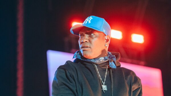 Rapero con gorra azul y micrófono en la mano sobre la tarima de Hip Hop al Parque en Bogotá, con luces rojas y pantalla de fondo