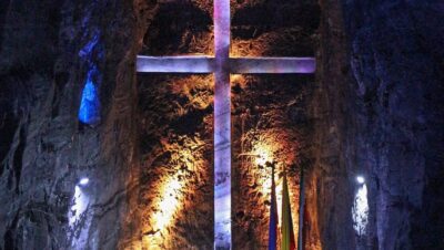 Nave central de la Catedral de Sal de Zipaquirá con una gran cruz iluminada tallada en la roca y bancas en primer plano