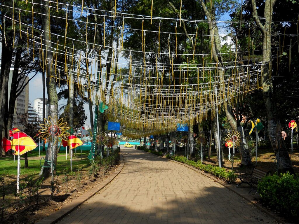 Calle peatonal del Parque de la Independencia en Bogotá decorada para Navidad con guirnaldas doradas colgadas entre los árboles y figuras de colores a los lados