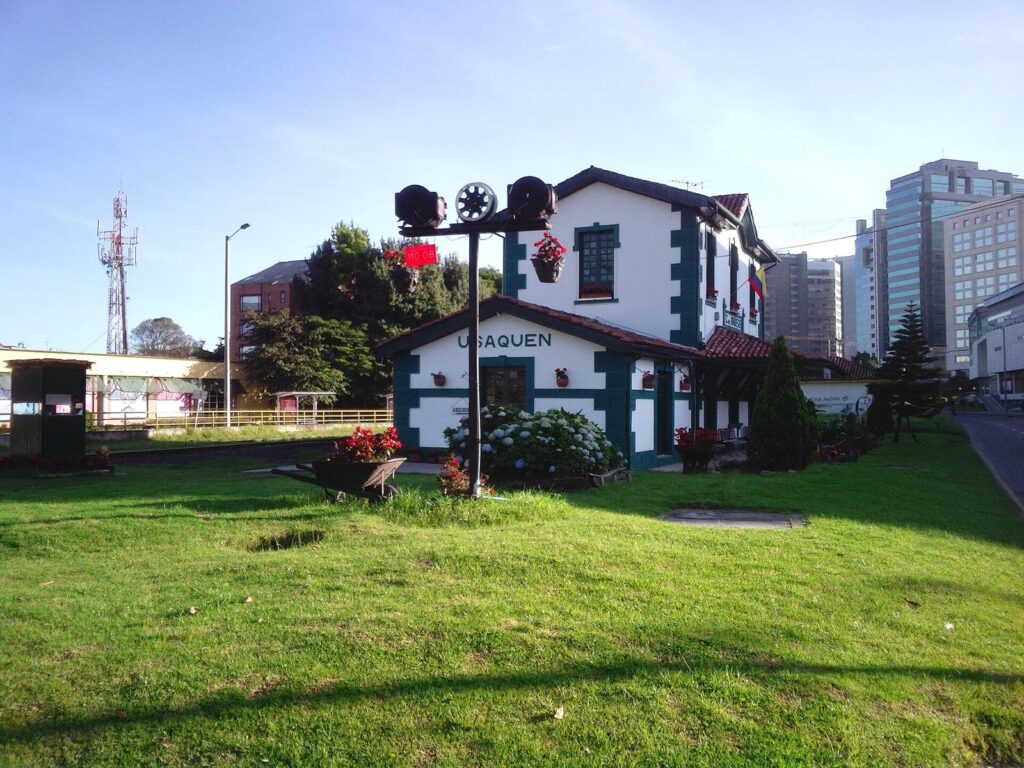 Estación del tren de Usaquén en Bogotá, una casa blanca de estilo europeo con jardín y edificios modernos al fondo