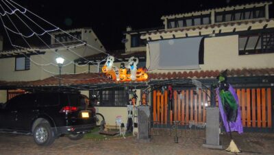 Fachada de una casa en Bogotá decorada de noche para Halloween con calabazas inflables, fantasmas, telarañas y una bruja