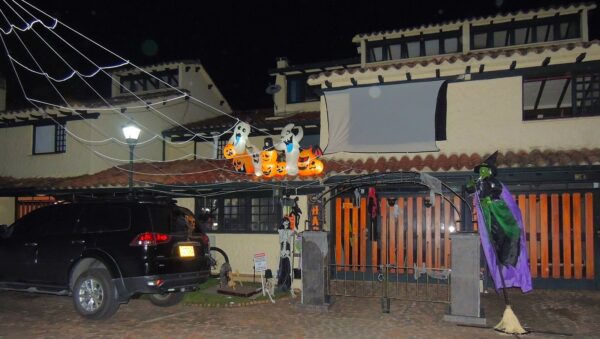 Fachada de una casa en Bogotá decorada de noche para Halloween con calabazas inflables, fantasmas, telarañas y una bruja