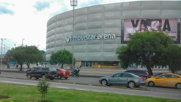 Fachada circular del Movistar Arena de Bogotá vista desde la avenida, con árboles y carros en primer plano