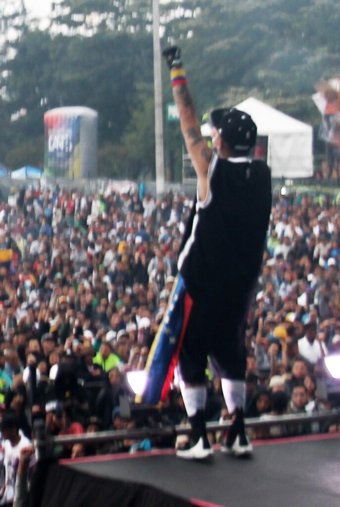 Rapero con el brazo en alto sobre la tarima de Hip Hop al Parque frente a una multitud en el Parque Simón Bolívar de Bogotá