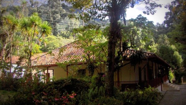 Casa colonial de la Quinta de Bolívar en Bogotá con techo de teja, rodeada de árboles y jardines al pie del cerro