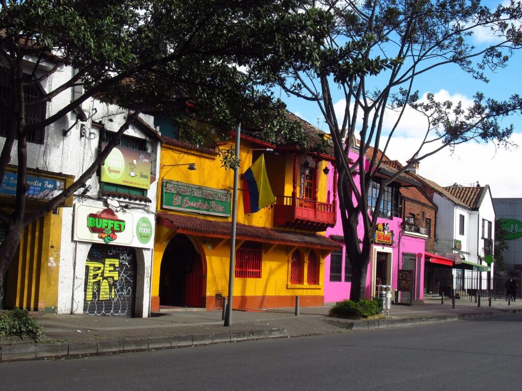 Bogotá Gourmet 2026: menús, precios y restaurantes 1 Fachadas coloridas de restaurantes en casas de dos pisos en la carrera 11 con calle 70, en Chapinero, Bogotá, con árboles y una bandera de Colombia