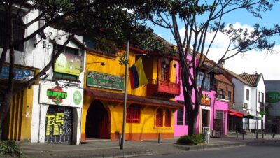 Fachadas coloridas de restaurantes en casas de dos pisos en la carrera 11 con calle 70, en Chapinero, Bogotá, con árboles y una bandera de Colombia