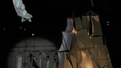 Espectáculo navideño nocturno en la Plaza de Bolívar de Bogotá con una acróbata suspendida en el aire y un gran barco de velas iluminado frente a un edificio histórico