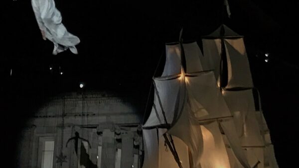 Espectáculo navideño nocturno en la Plaza de Bolívar de Bogotá con una acróbata suspendida en el aire y un gran barco de velas iluminado frente a un edificio histórico